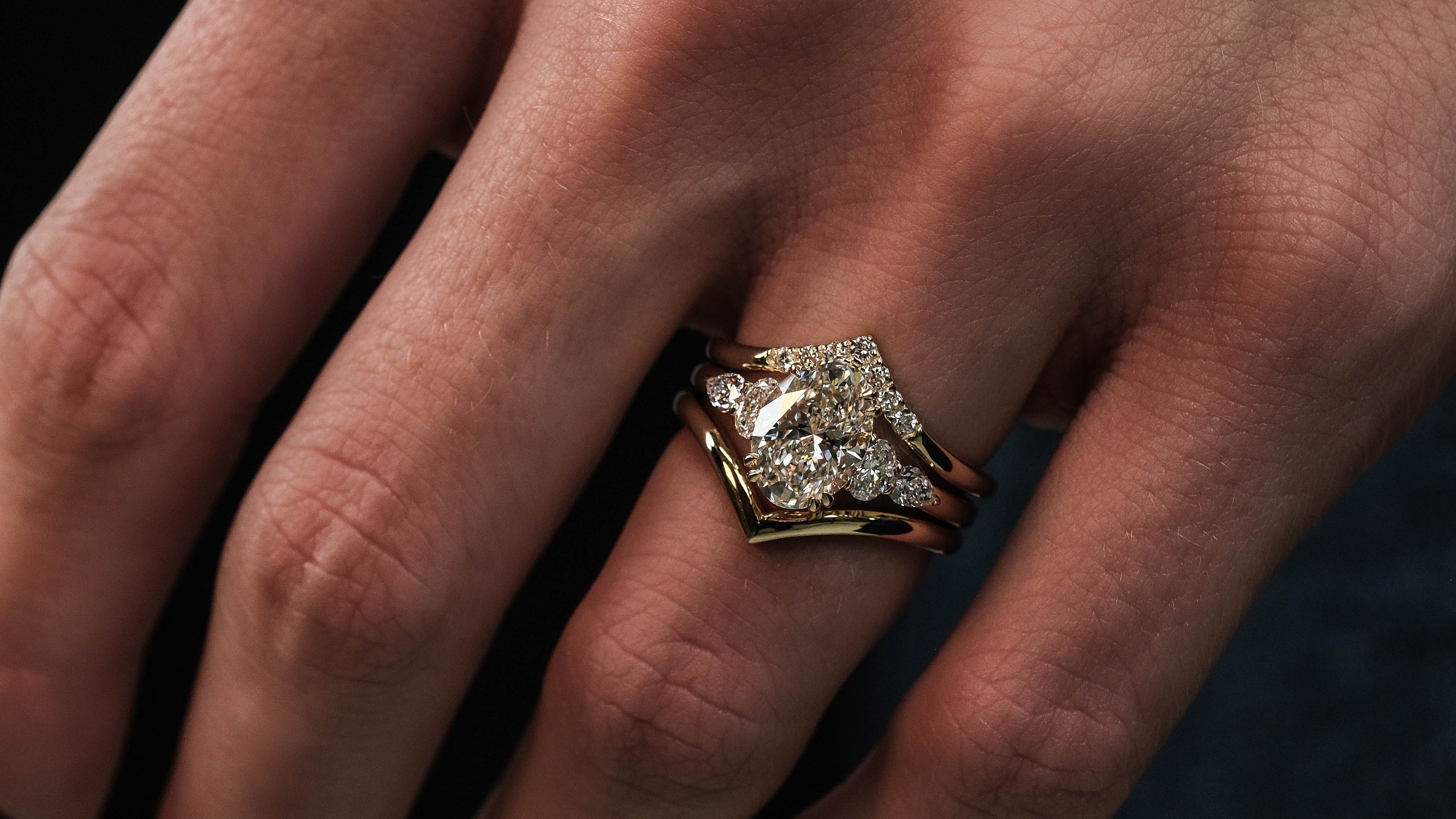Close-up of a hand wearing a diamond ring on a dark background