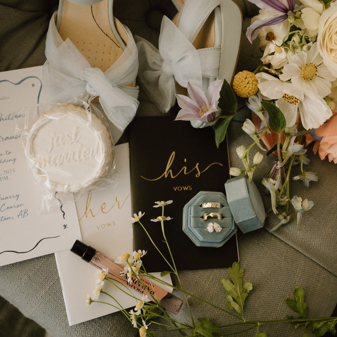 White wedding shoes with bows, 'just married' sign, and bouquet on a green cushion.