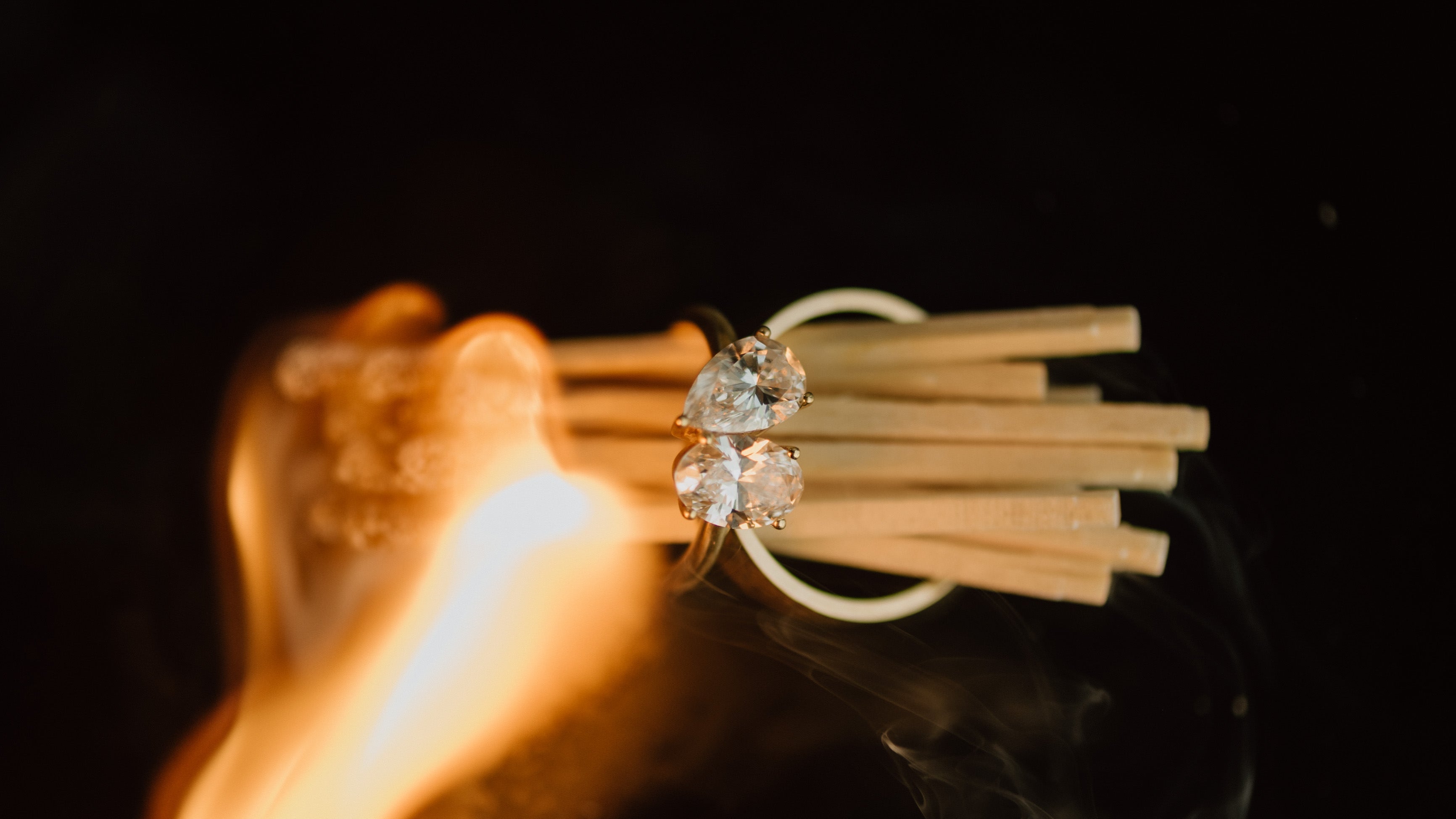 Diamond ring held above flames on a black background